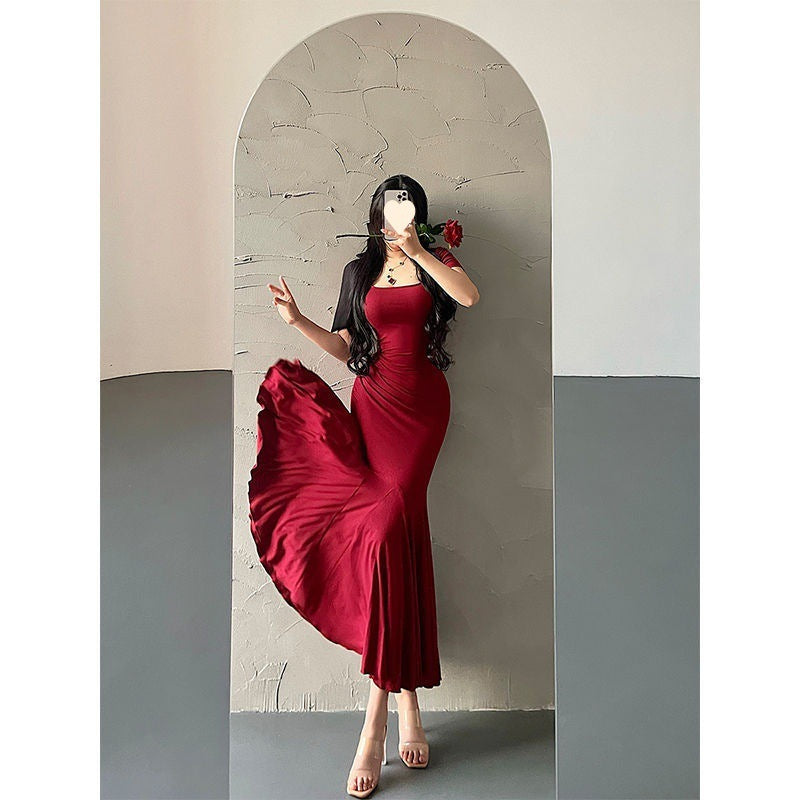 Woman in a red dress taking a mirror selfie against a plain wall.