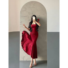 Woman in a red dress taking a mirror selfie against a plain wall.