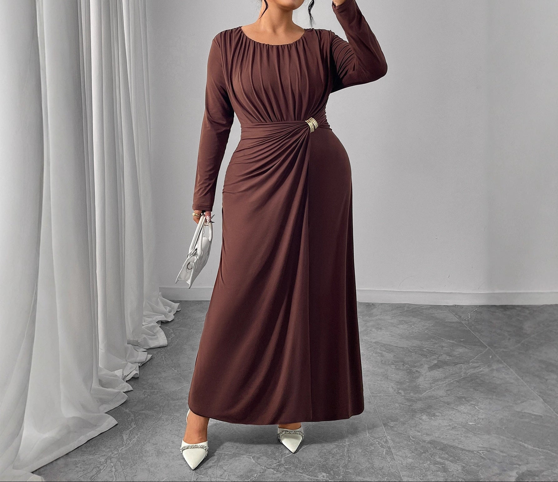 Woman in a brown dress holding a phone and a clutch against a gray background