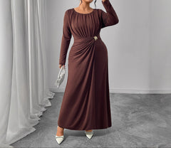 Woman in a brown dress holding a phone and a clutch against a gray background