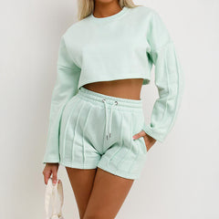 Person wearing a light green sweatshirt and shorts set on a plain background