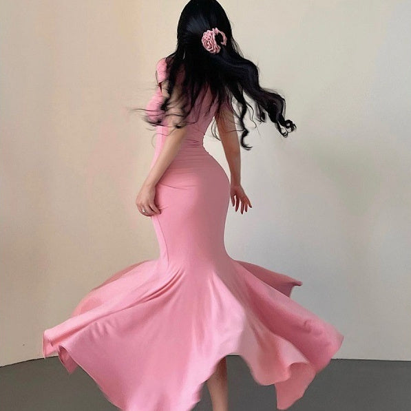 Woman wearing a pink mermaid-style dress against a plain background