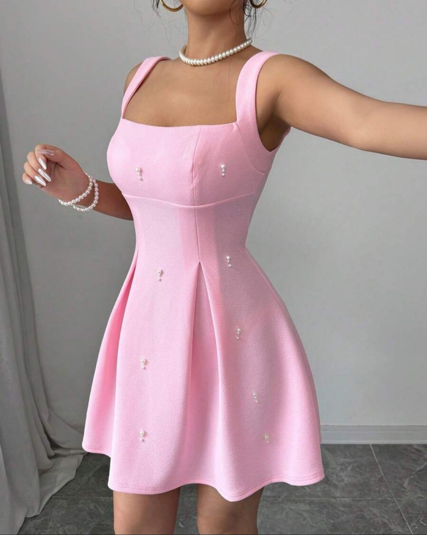 Pink dress with pearl embellishments worn by a model against a neutral background