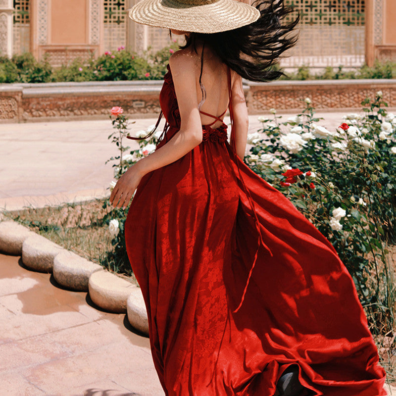 Woman in a red dress with a wide-brimmed hat walking through a garden.