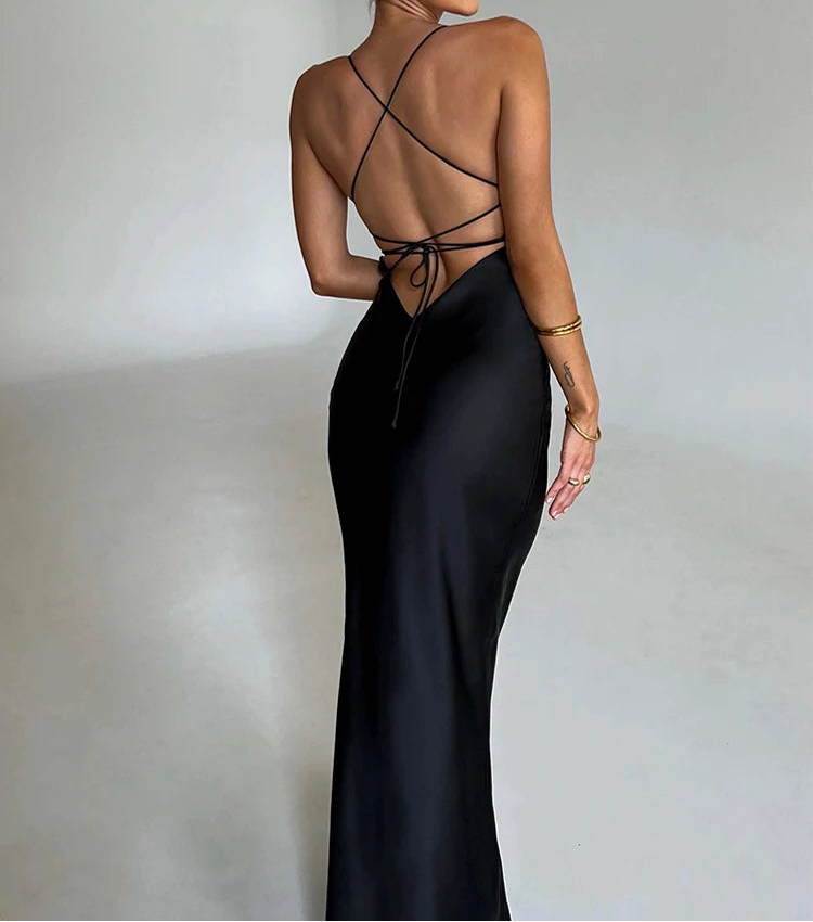 Woman wearing a black evening gown with a strappy back design on a plain background