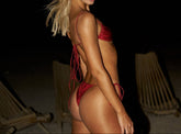 Woman in a red bikini standing on a beach with lounge chairs in the background