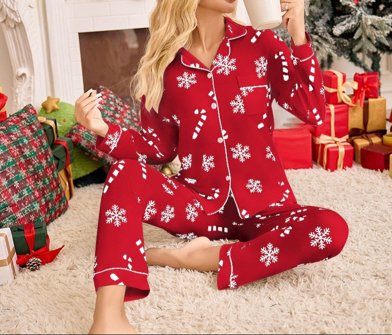 Woman in red Christmas pajamas with white snowflake patterns, sitting on a carpeted floor with a decorated fireplace and tree in the background.