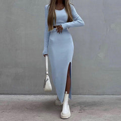 Woman wearing a light blue long-sleeve top and skirt with white boots against a gray wall.