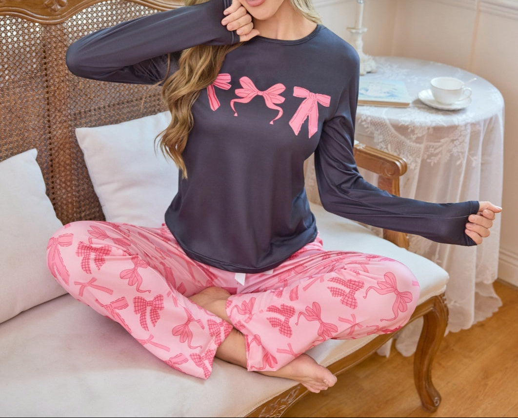 Woman wearing a dark purple long-sleeve top and pink pajama pants with bow patterns, sitting on a couch.