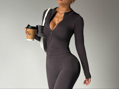 Woman in a dark gray outfit holding a coffee cup against a plain background