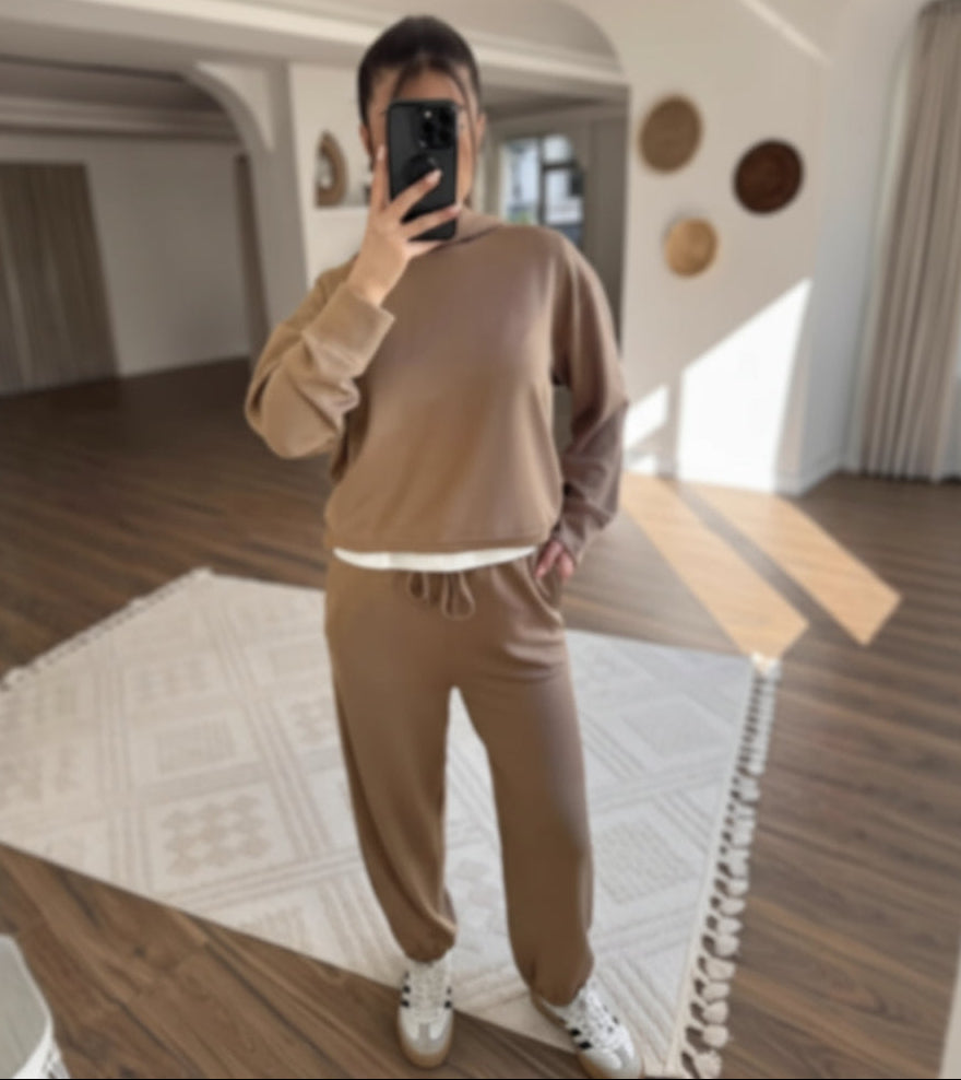 Person taking a mirror selfie wearing a brown outfit in a modern room.