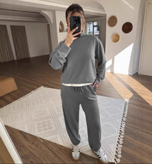 Person wearing a gray tracksuit taking a mirror selfie in a room with wooden flooring and decorative wall items.
