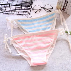 Two striped bikini bottoms on a textured surface with glasses and books in the background.