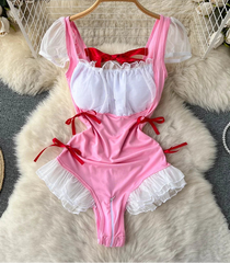 Pink and red swimsuit with lace details on a hanger against a textured surface.