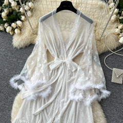 White lace robe with feather details on a hanger against a decorative background.