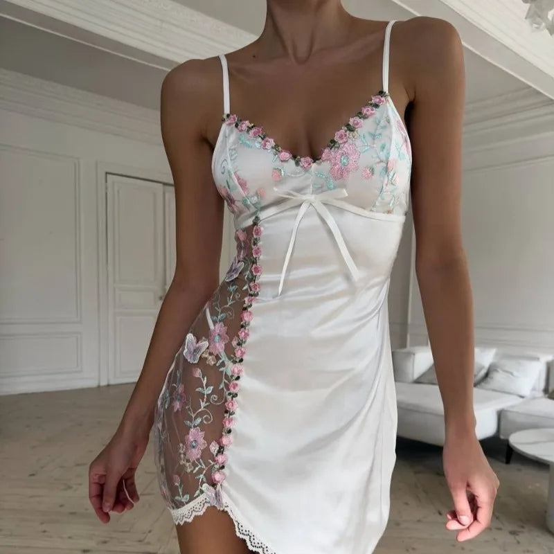 Woman wearing a white slip dress with floral embroidery in a room.