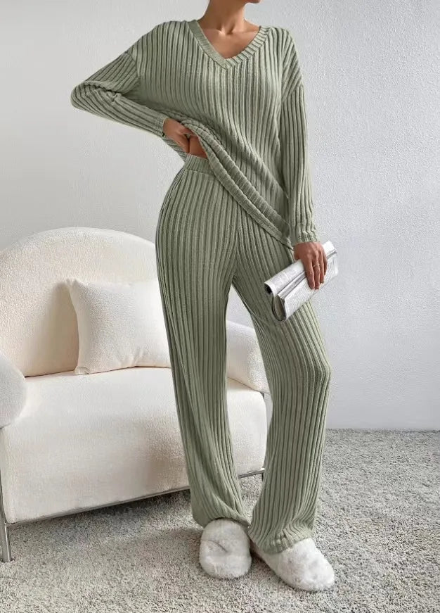 Person wearing a green ribbed knit outfit sitting on a white couch.