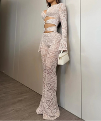 Woman in a white lace outfit standing against a neutral wall.