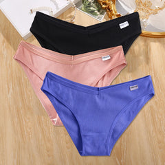 Three pairs of underwear in black, pink, and blue on a wooden surface.
