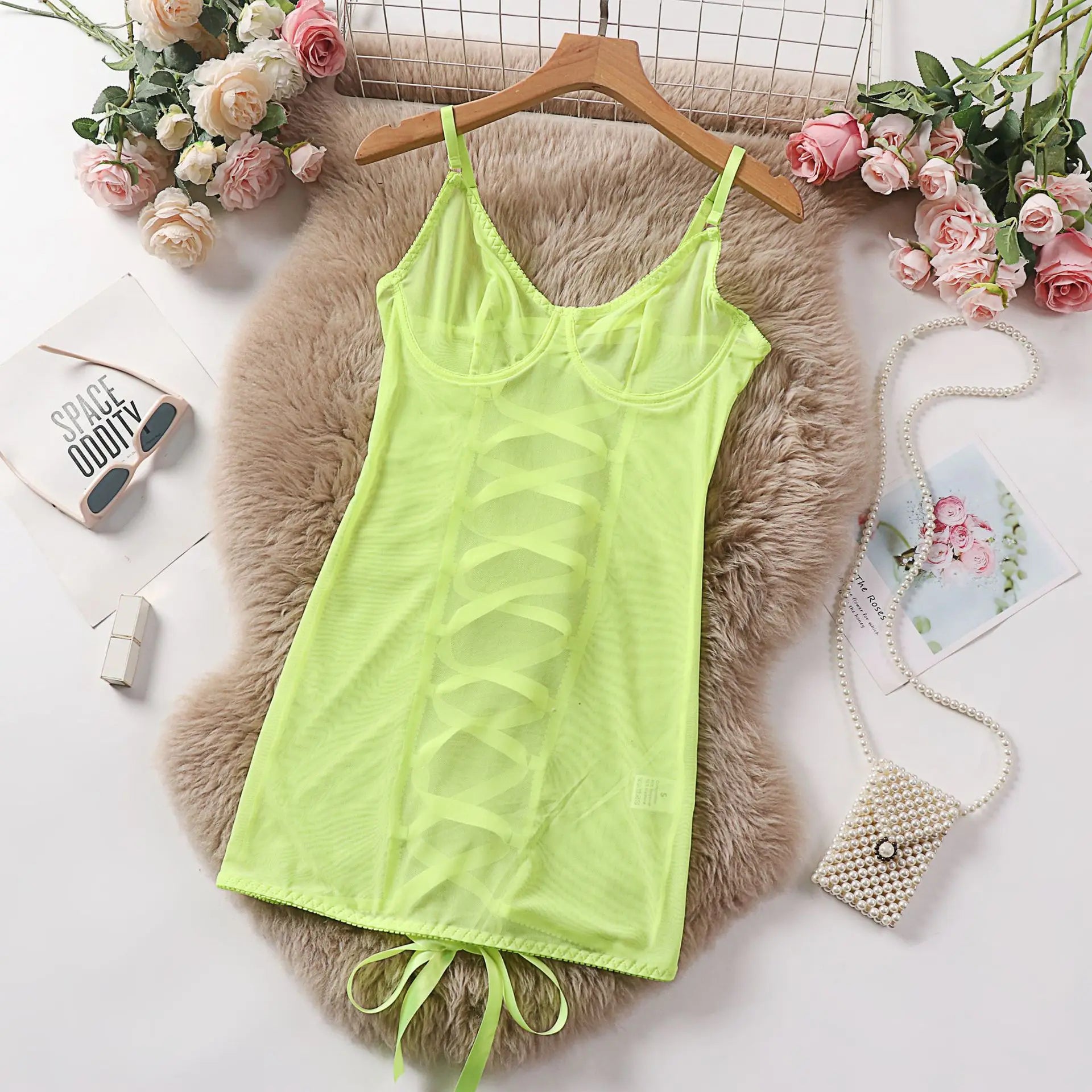 Lime green tank top on a hanger with decorative flowers and fluffy pillow in the background