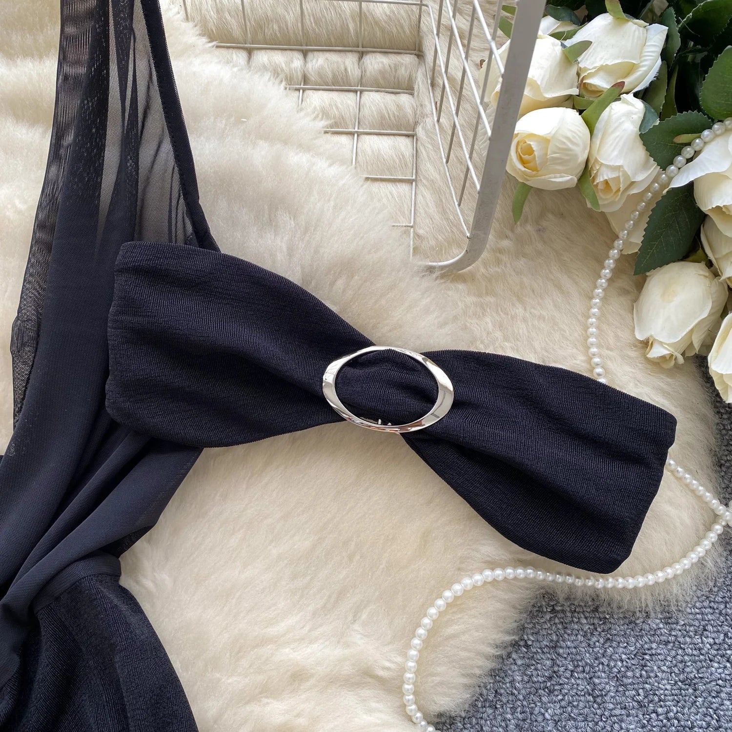 Black bikini top with a large bow and silver ring on a textured surface with flowers and pearls.