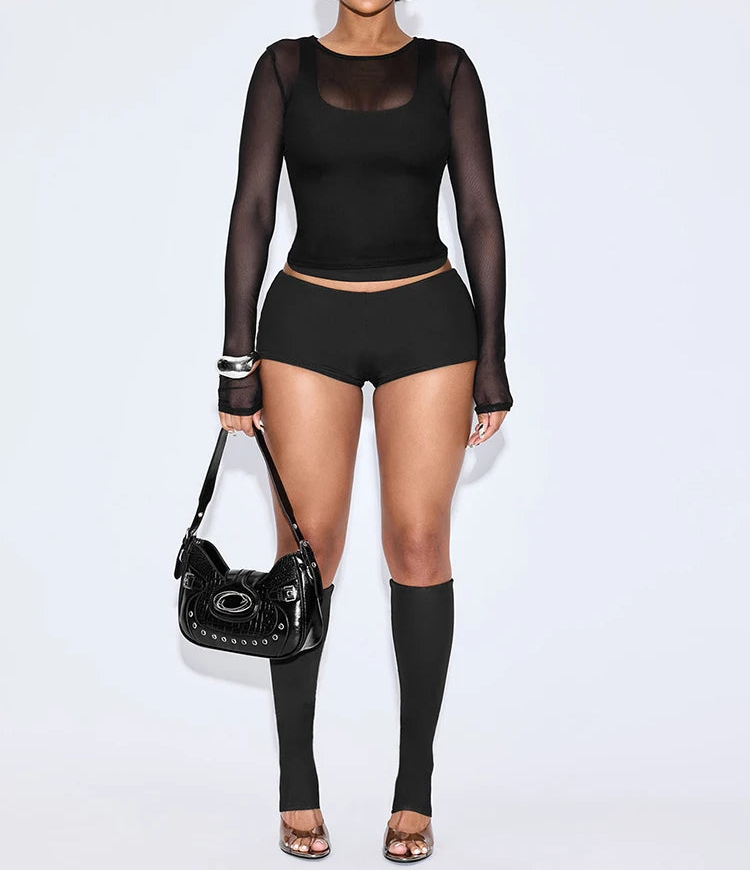 Person wearing a black outfit with sheer sleeves and high-waisted shorts, holding a black handbag on a white background.