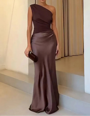 Woman in a brown one-shoulder evening gown standing on a staircase.