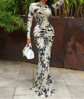 Woman in a black and white floral dress standing outdoors with greenery in the background