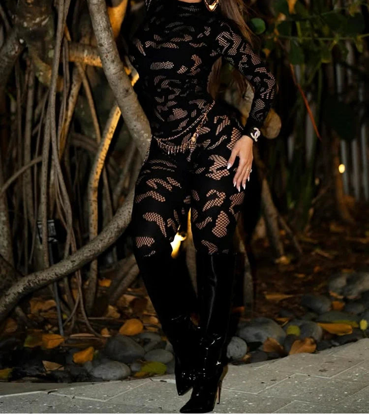 Woman in a black lace outfit standing in a natural setting with plants and rocks.