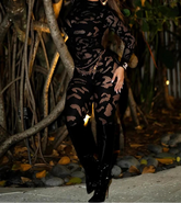 Woman in a black lace outfit standing in a natural setting with plants and rocks.