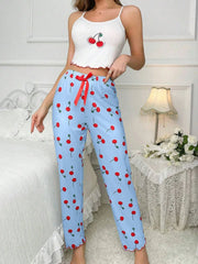 Woman wearing a white crop top with cherry design and blue pants with red cherry pattern in a bedroom setting.
