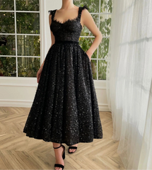 A woman wearing a black sequin party dress with a v-neckline and open back, standing by a window.