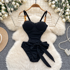 Black swimsuit with a bow on a hanger against a decorative background with flowers and a hat.