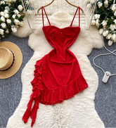 Red dress with ruffles on a white fur rug surrounded by flowers and a hat.