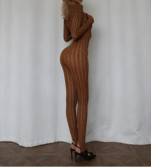 Woman wearing a brown ribbed knit outfit standing against a white curtain.