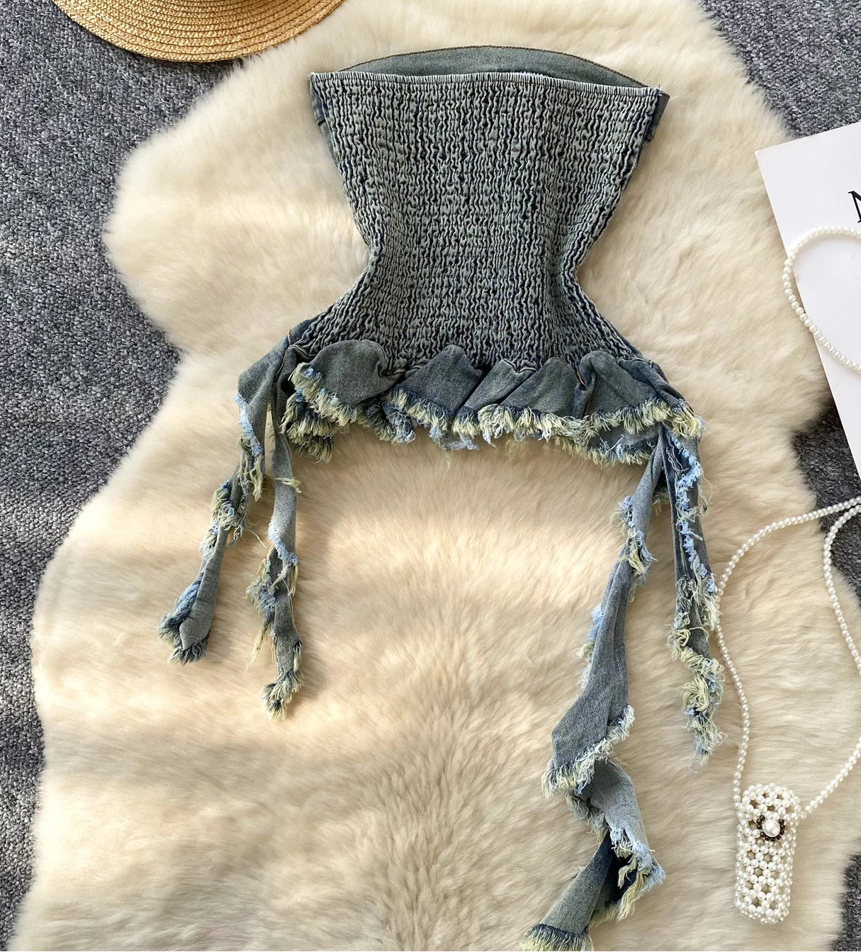 Denim bikini top with tassels on a fur surface with a hat and card in the background