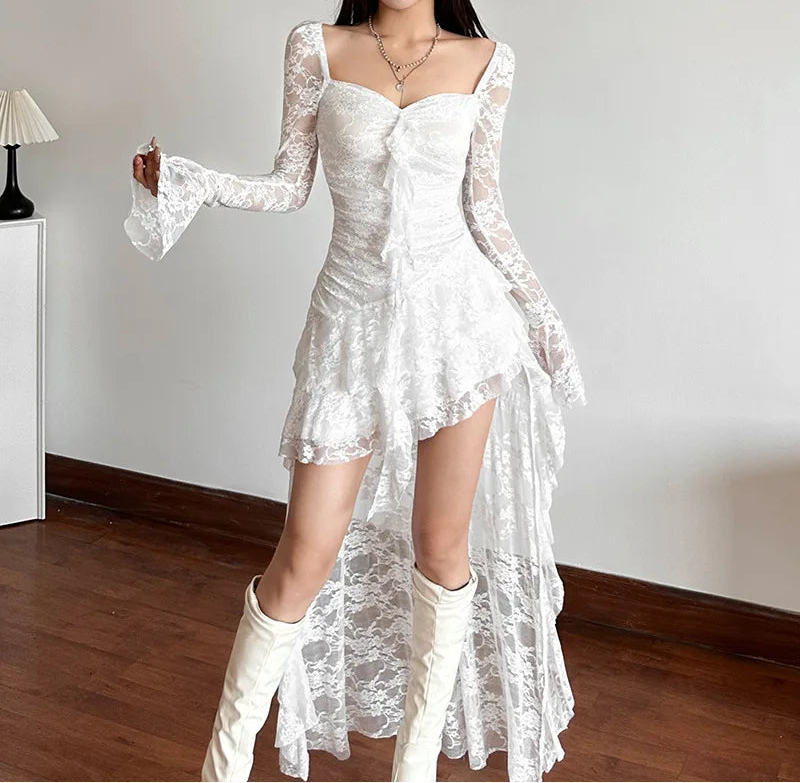 Woman wearing a white lace dress with long sleeves and high-low hem in a room.