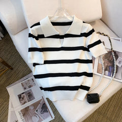 Black and white striped sweater on a hanger with a magazine and handbag on a couch.