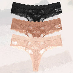Three pairs of lace underwear in black, rose gold, and pink on a textured gray background.
