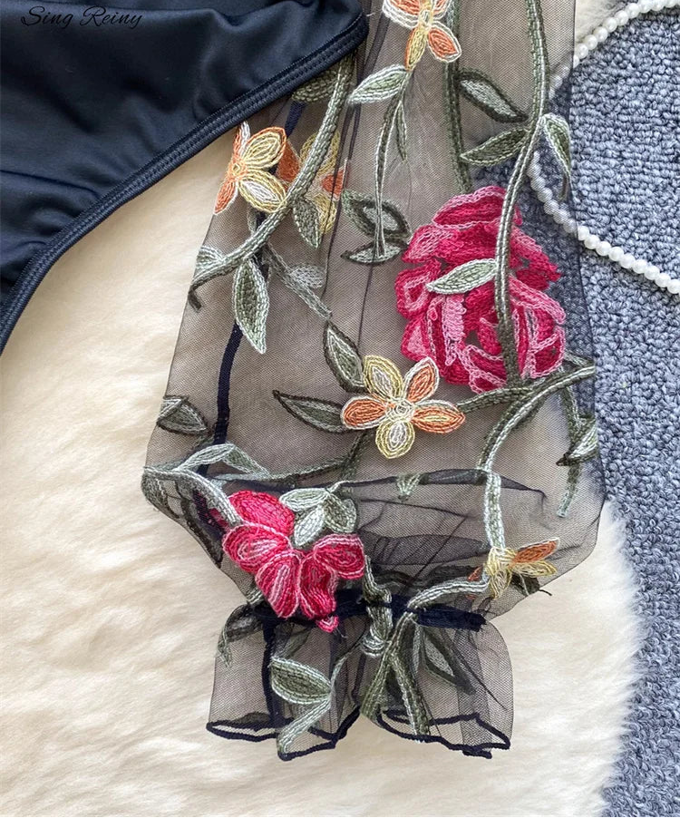 Embroidered floral scarf with pink roses and green leaves on a textured surface