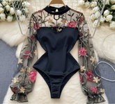 Black swimsuit with floral lace overlay on a white surface