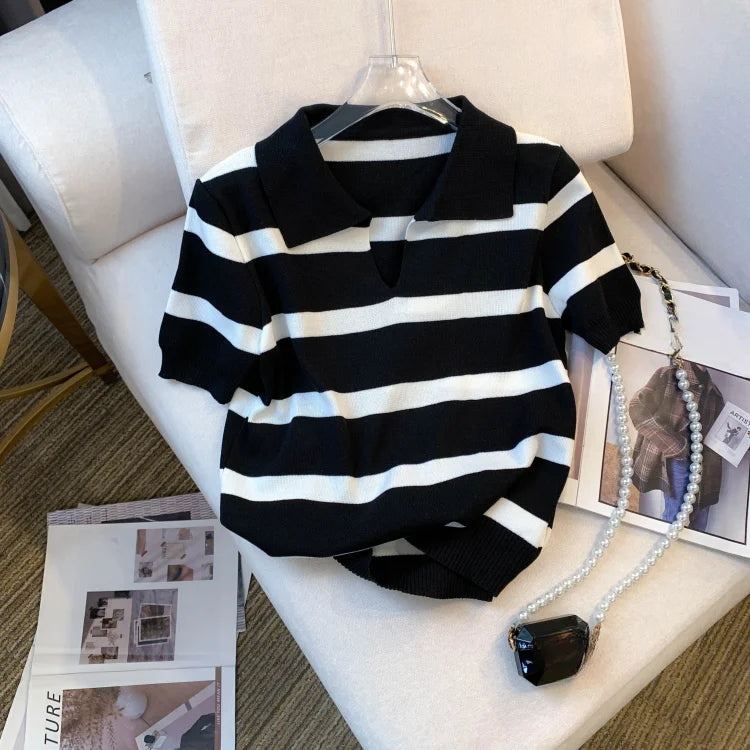 Black and white striped sweater on a hanger with a necklace on a chair.