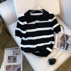 Black and white striped sweater on a hanger with a necklace on a chair.
