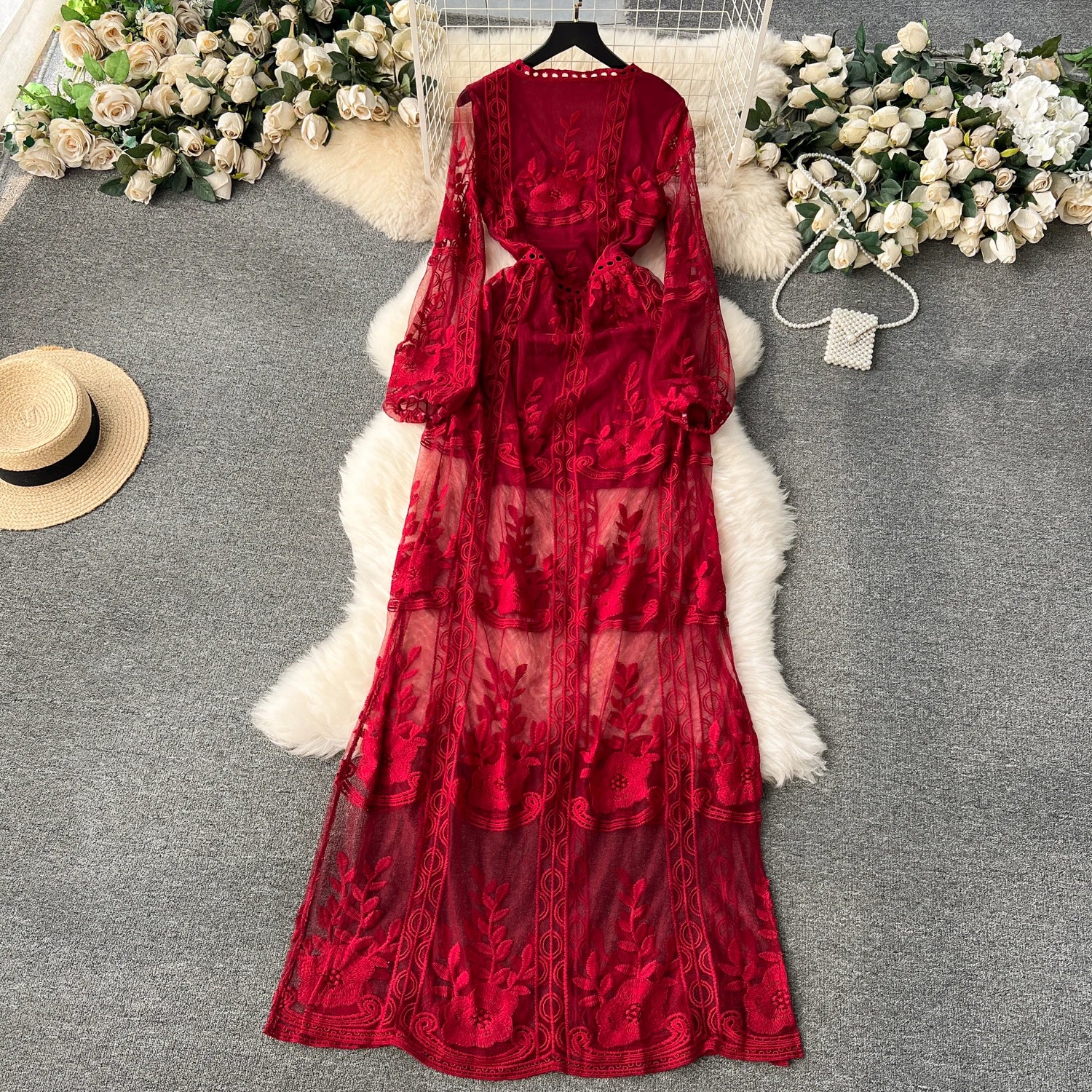 Red lace dress on a gray surface with flowers and a hat in the background
