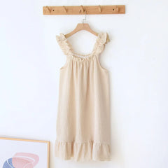 Beige dress with ruffled details hanging on a wooden hanger against a white wall.