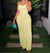 Woman in a yellow dress holding a green clutch against a dark background with plants.