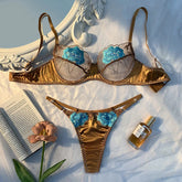 Gold bra set with blue floral details on a textured surface with a book and flower.