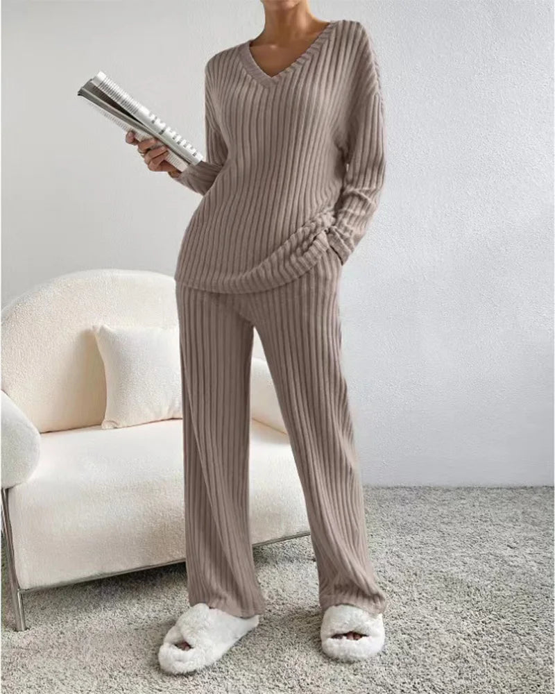 Person wearing a beige ribbed lounge set with white fluffy slippers, holding a book in a living room.