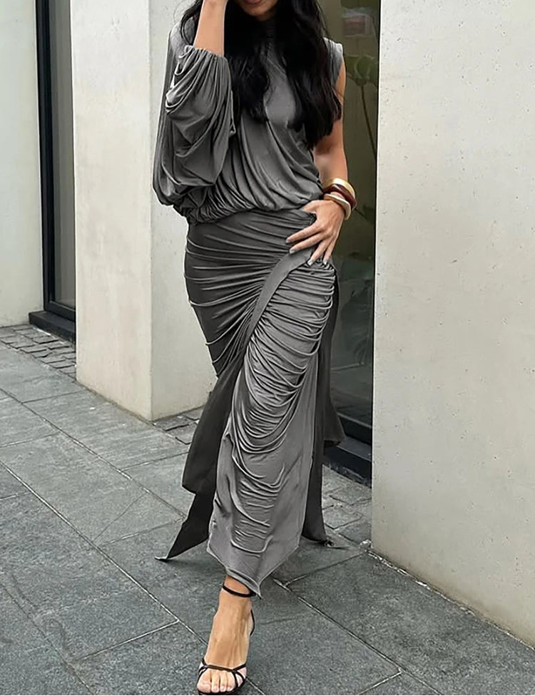 Woman wearing a gray ruched dress standing against a building wall.