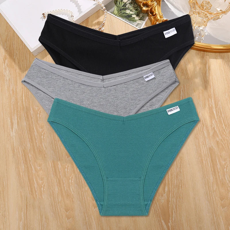 Three pairs of underwear in black, gray, and green on a wooden surface.